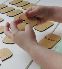 Hands interacting with wooden puzzle pieces on a white surface