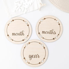 Three round wooden plates with engraved text 'month', 'months', and 'year' on a white background.