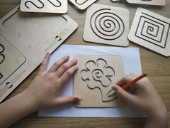 Wooden cutout shapes on a table with hands using a pencil