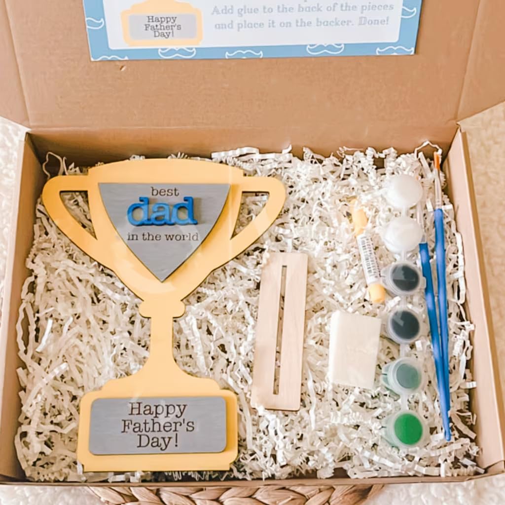 Craft kit with wooden plaque, paint bottles, and brushes in a box labeled 'Happy Father's Day'.
