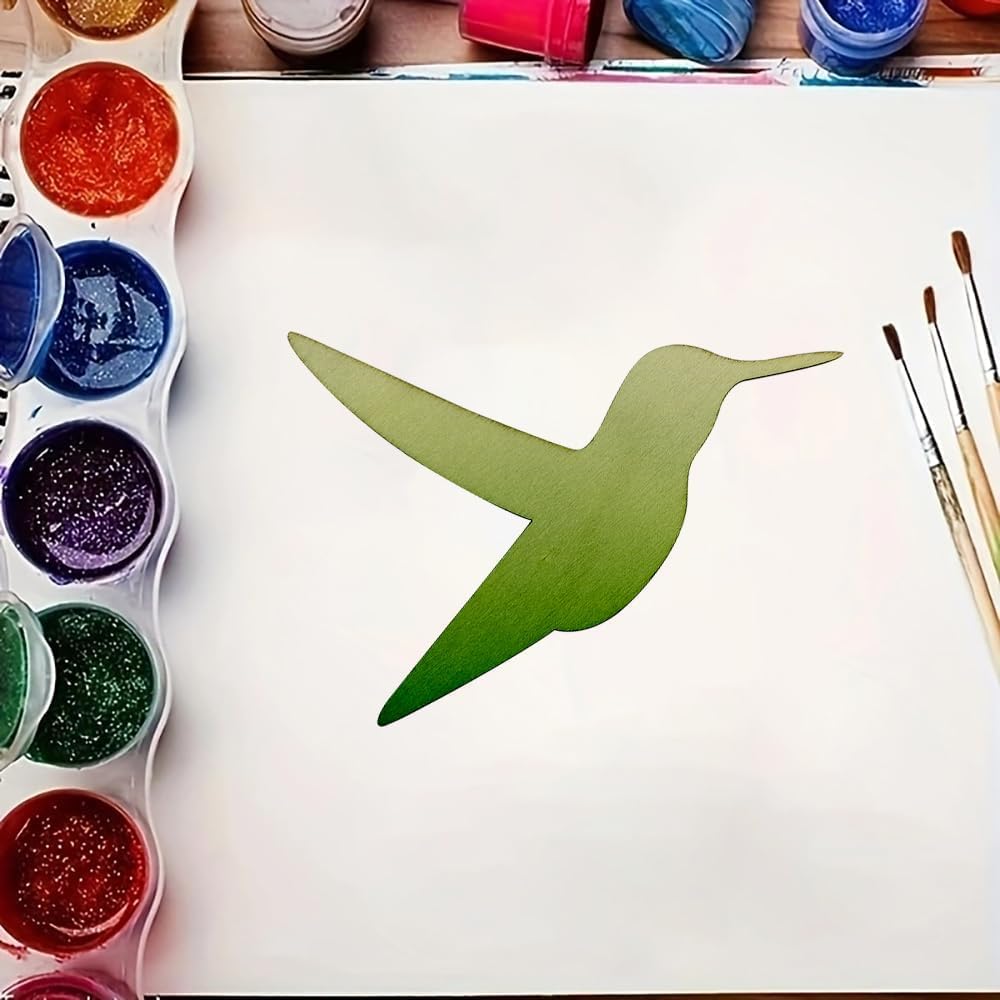 Green paper cutout of a hummingbird on a white sheet with paint containers and brushes.