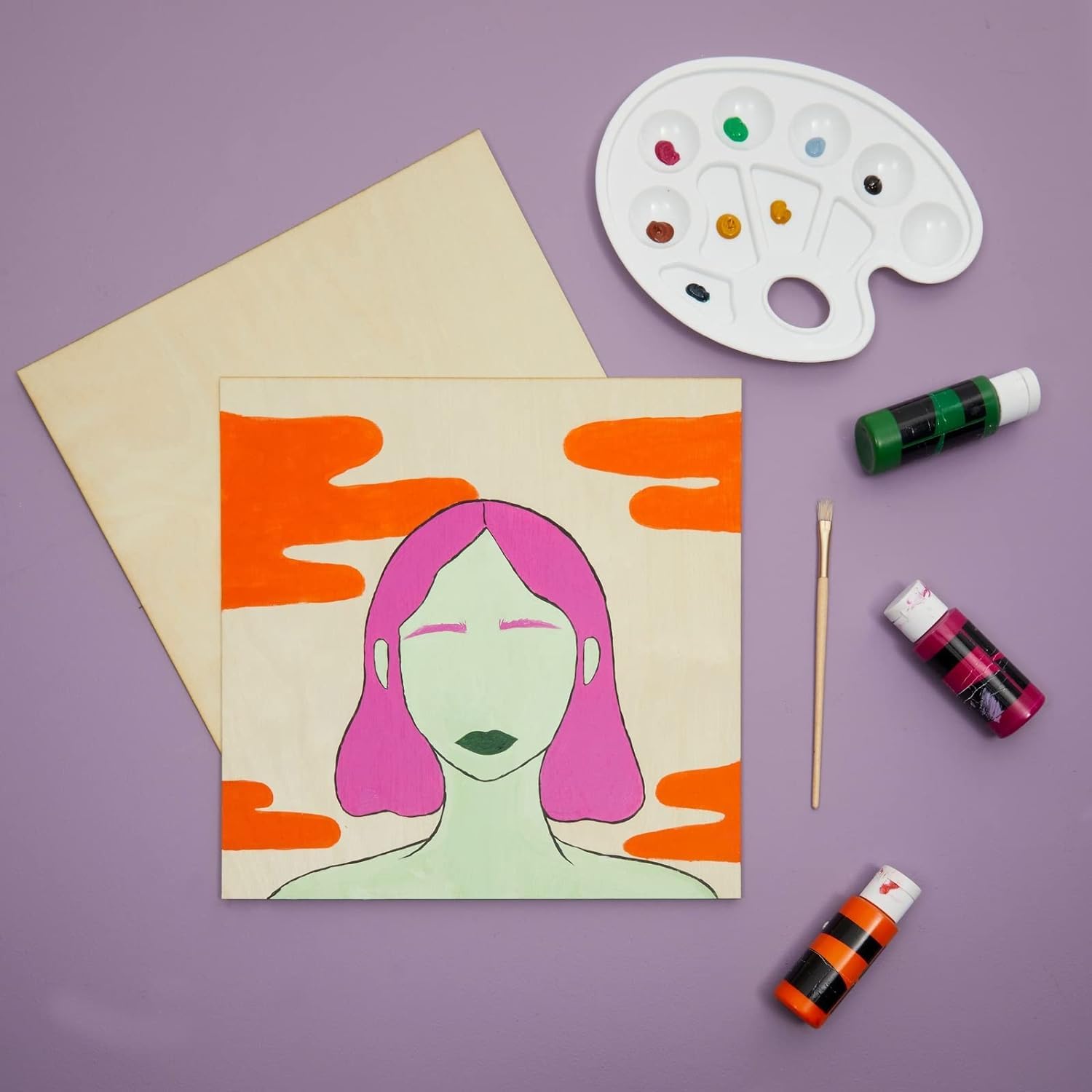 Artistic depiction of a woman with pink hair on a beige card, surrounded by art supplies on a purple background.