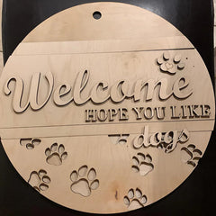 Wooden round sign with 'Welcome hope you like dogs' text and paw prints on a black background