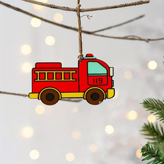 Red fire truck ornament hanging on a branch with a blurred light background