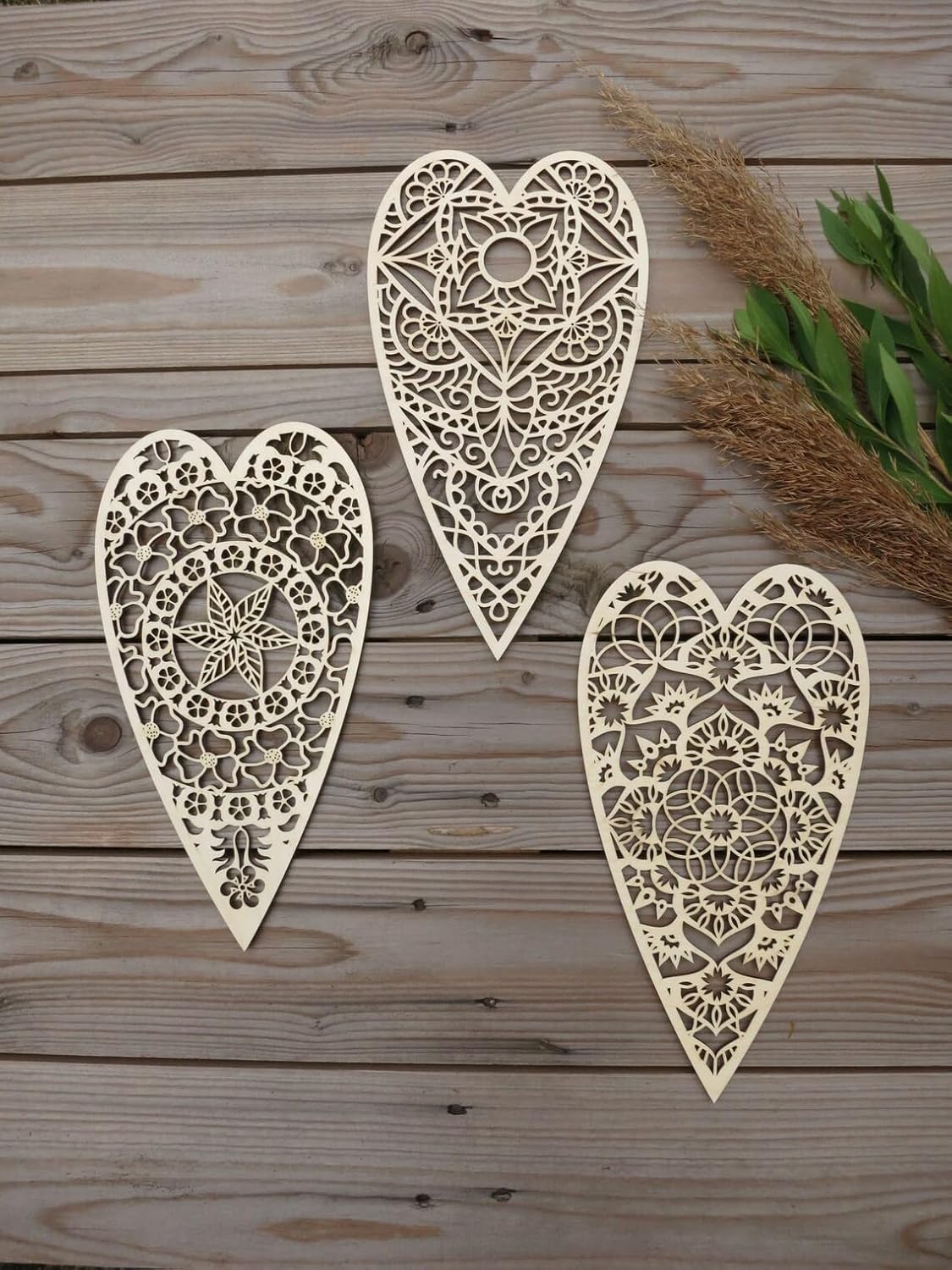 Three ornate heart-shaped wooden decorations on a wooden surface with greenery.