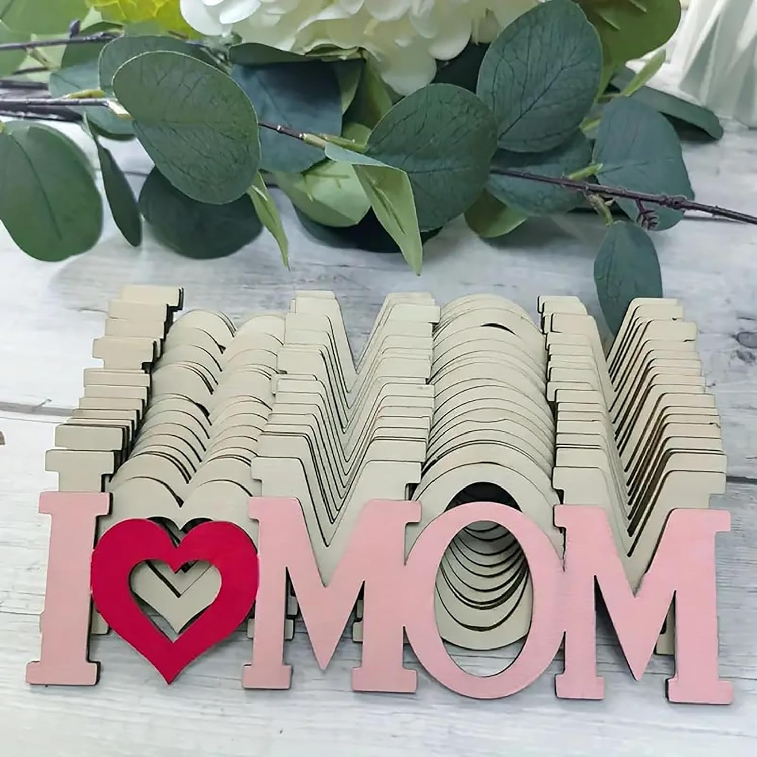 Wooden letters spelling 'I ❤️ MOM' with green leaves in the background