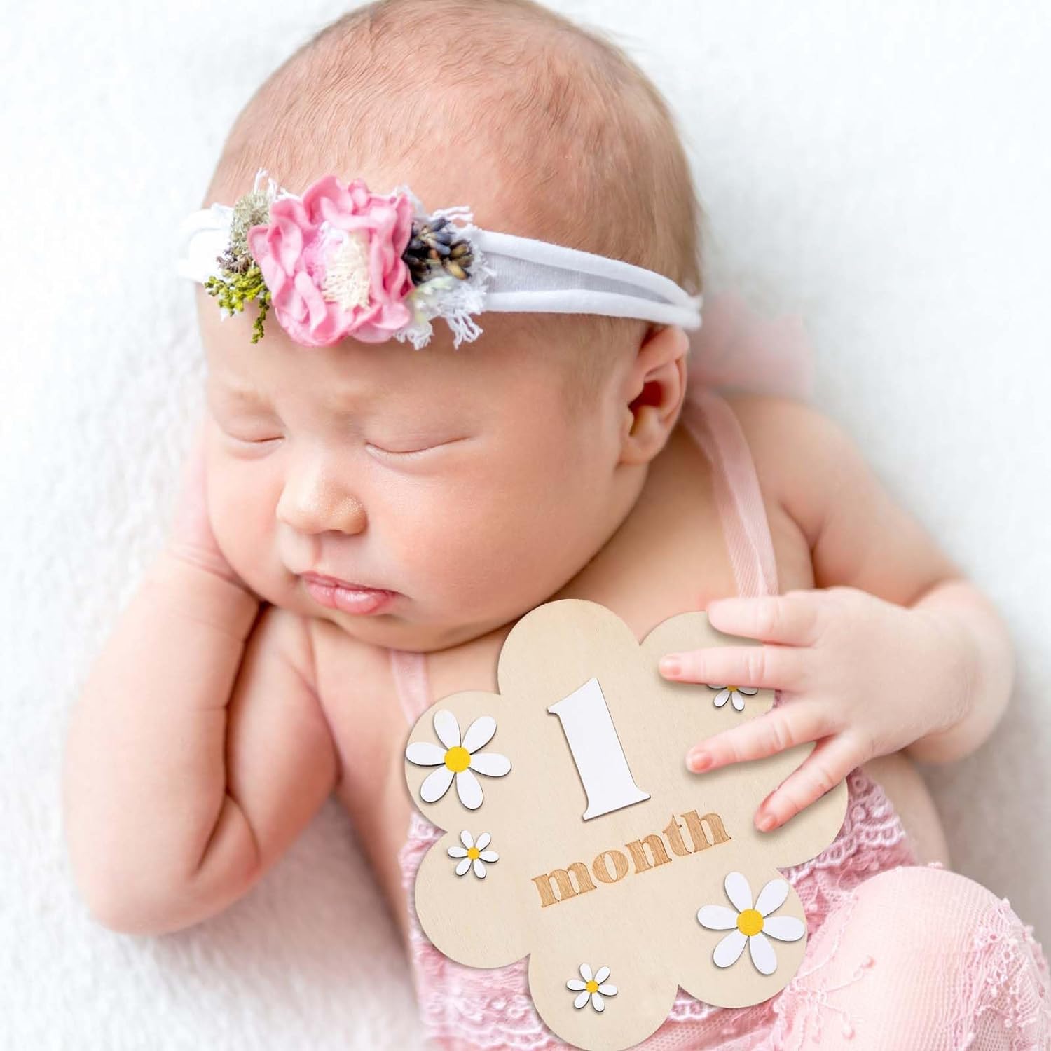 Baby wearing a floral headband and holding a '1 month' sign against a white background