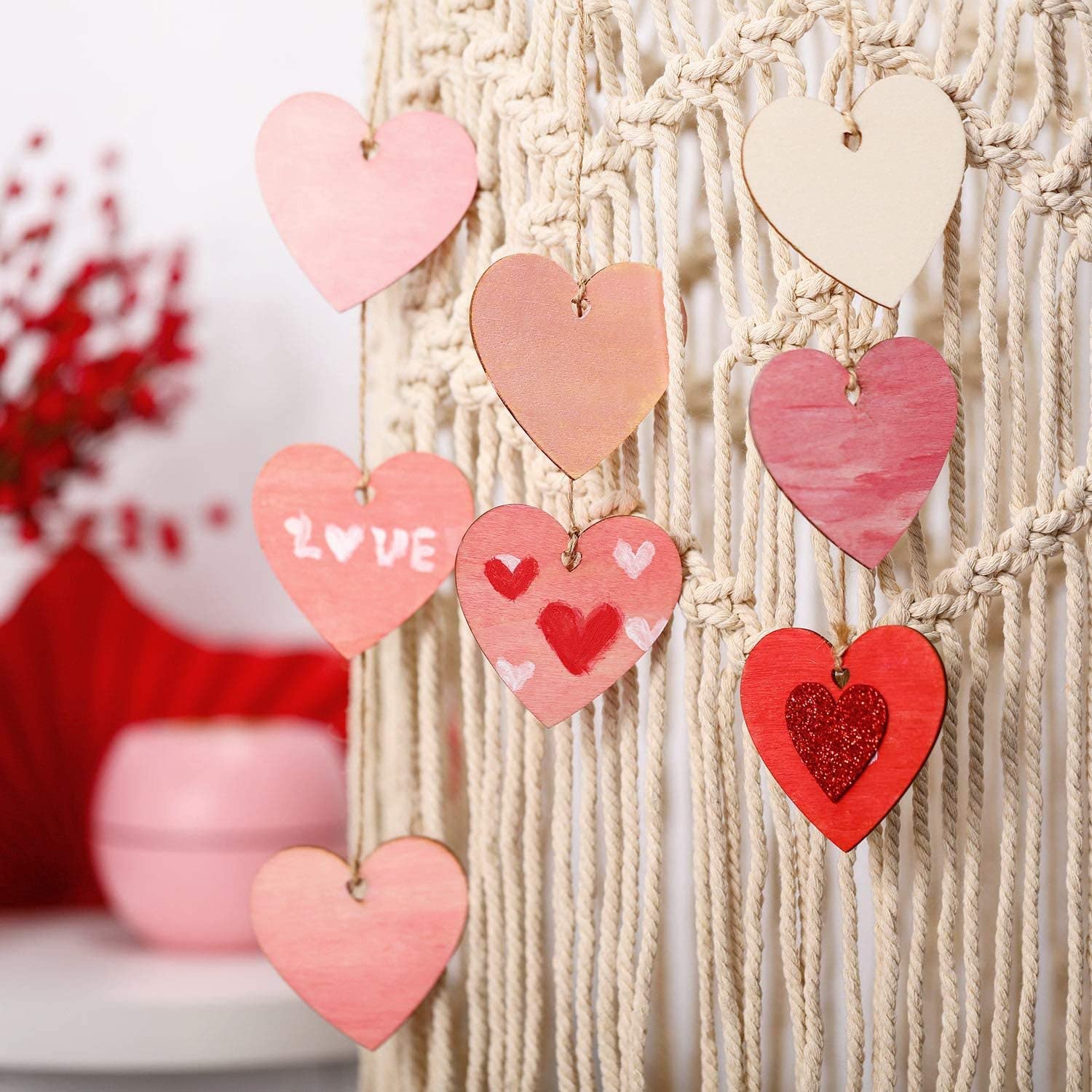 Decorative heart-shaped ornaments hanging on a macrame wall with a blurred background.