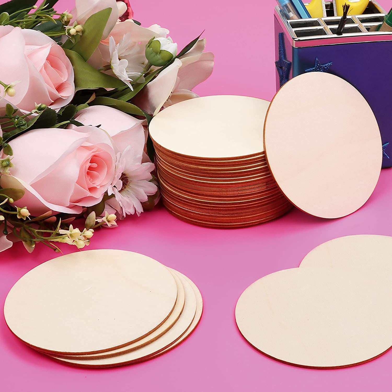 Stacks of round wooden coasters on a pink surface with flowers and a purple box in the background.