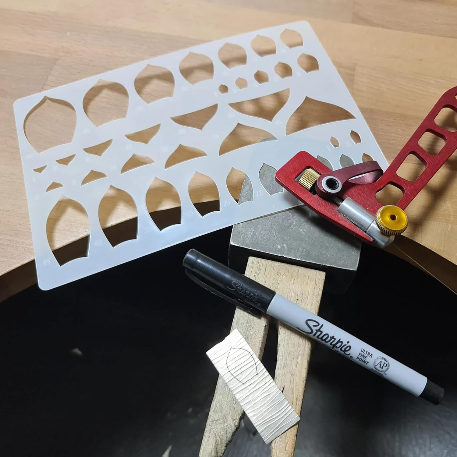 Metal template with cut-out shapes, red tool, and Sharpie marker on a wooden surface