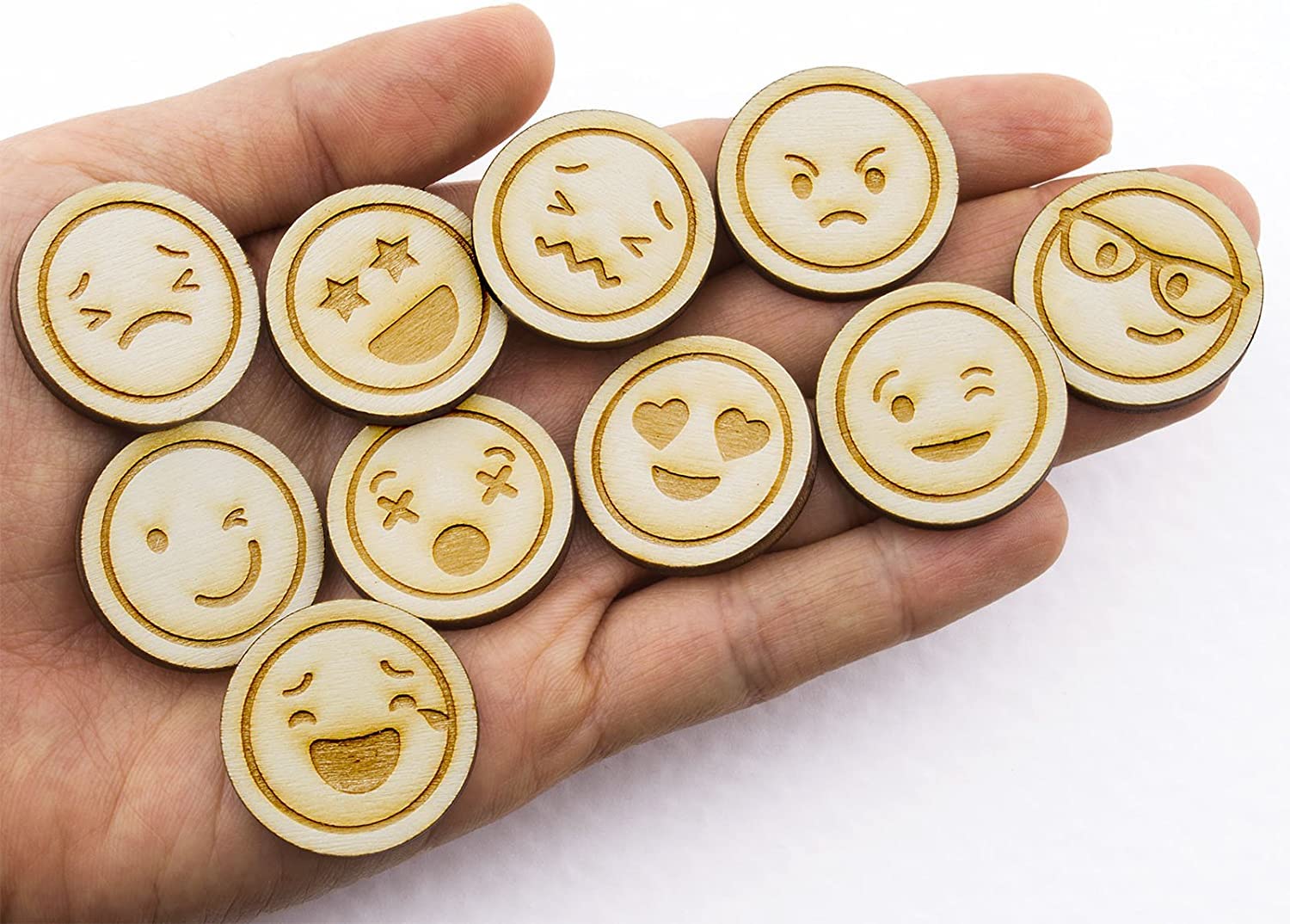 Wooden emoji buttons with various expressions held in a hand against a white background
