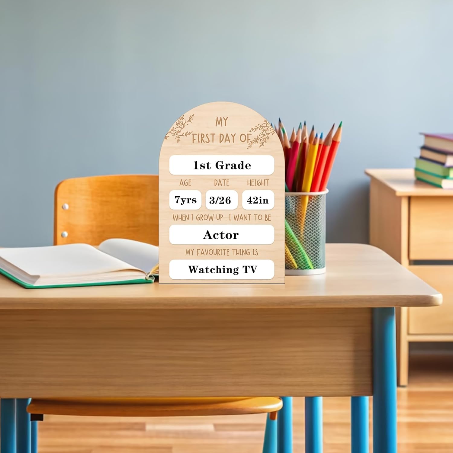 Wooden plaque on a school desk with stationery, against a gray wall.