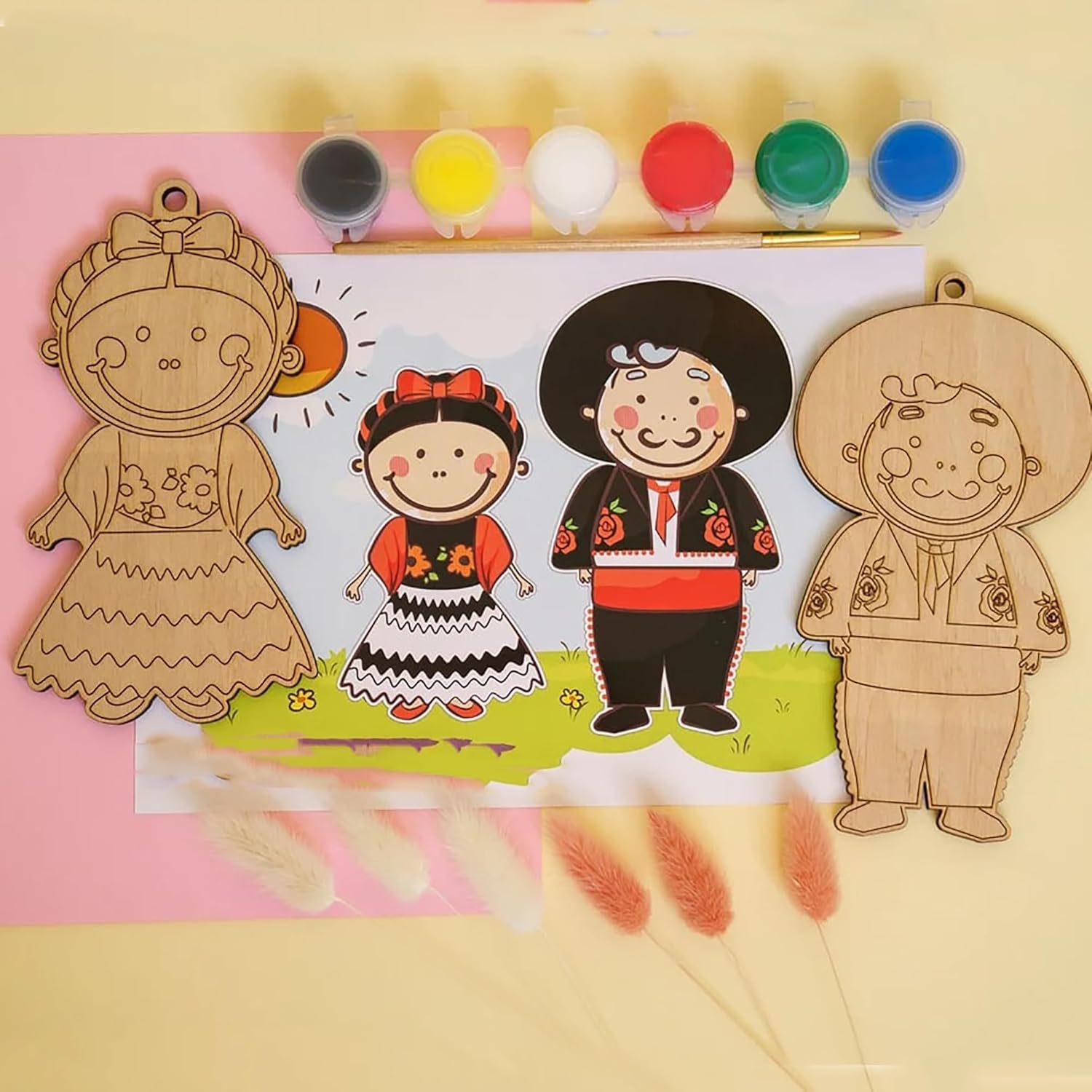 Wooden cutouts of dolls in traditional outfits with paint bottles on a pink background