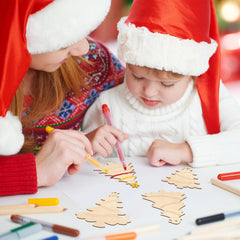Children wearing Santa hats coloring wooden Christmas tree crafts with markers.