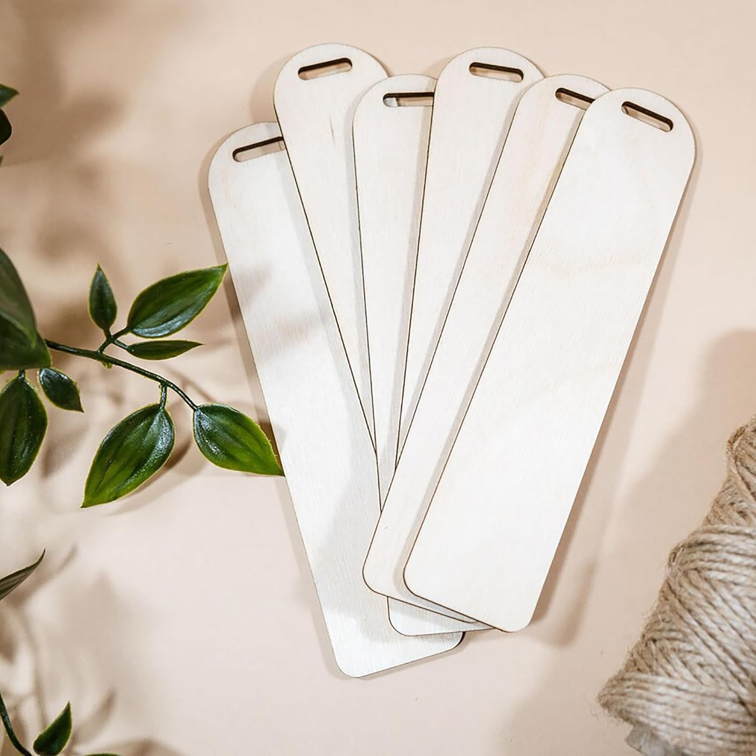 Set of white bookmarks on a beige surface with green leaves and twine