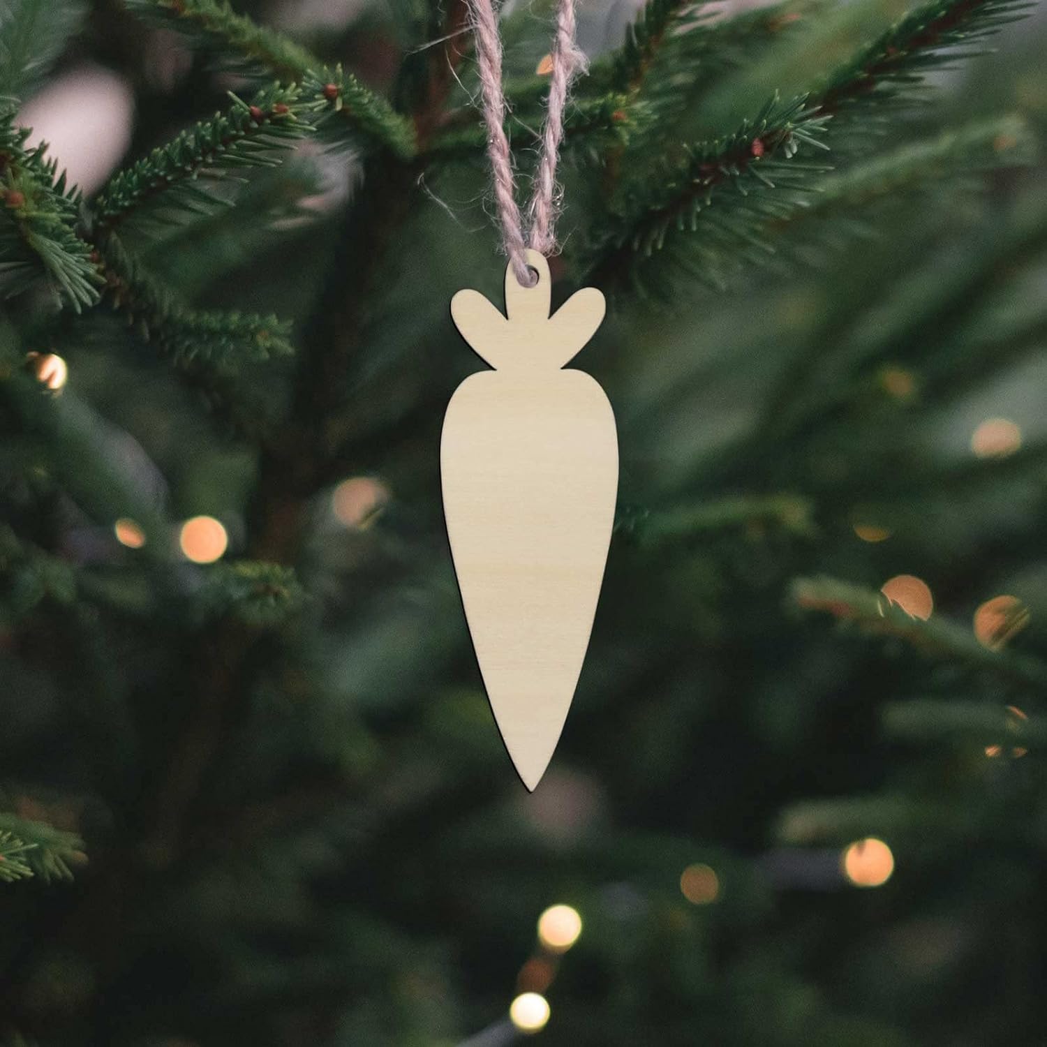 Wooden carrot ornament hanging on a Christmas tree with blurred lights in the background