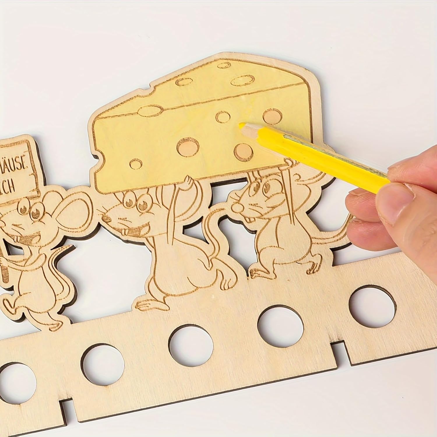 Wooden puzzle with mice and cheese design, held by a hand with a yellow pencil.