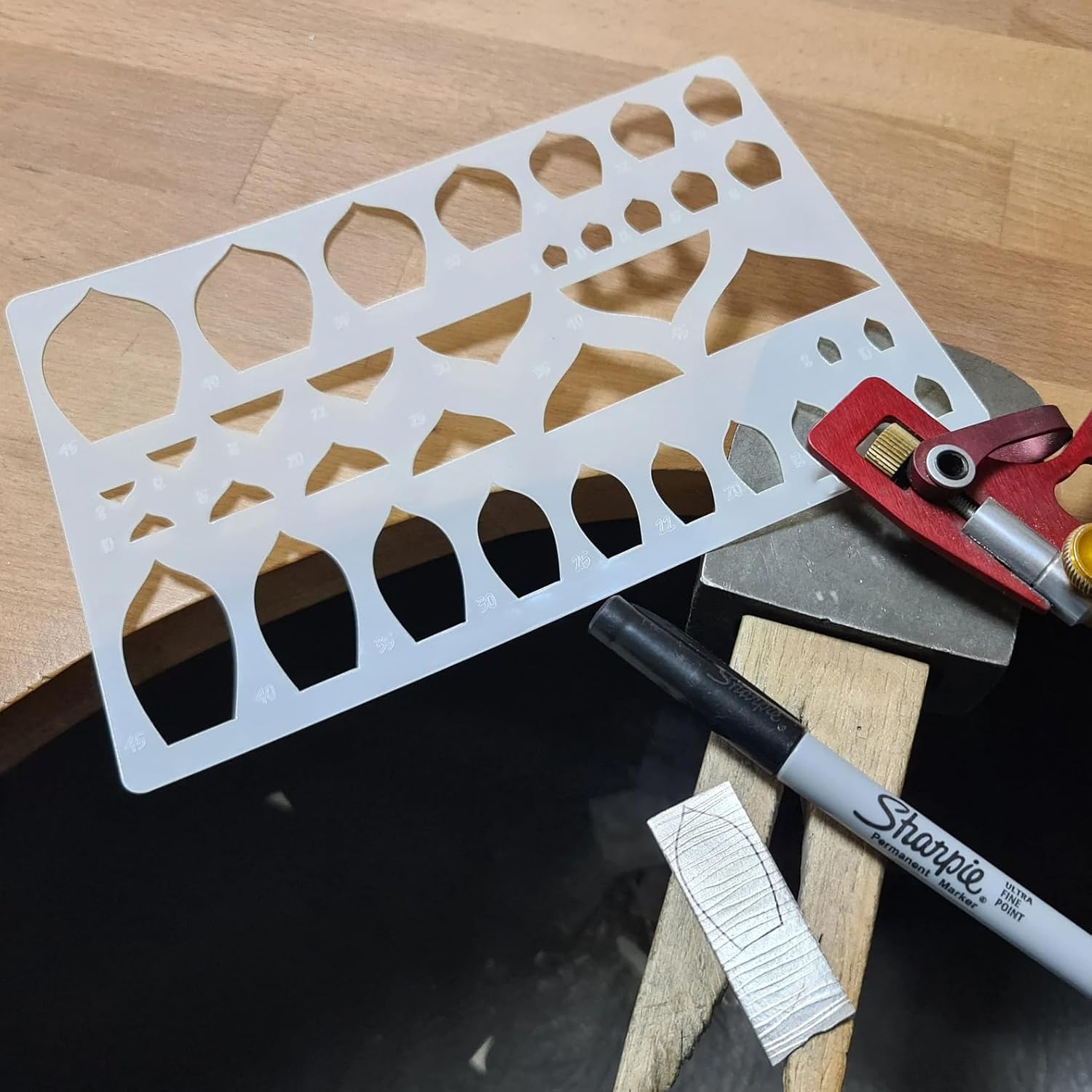 Metal template with cut-out shapes on a wooden surface with a Sharpie marker.