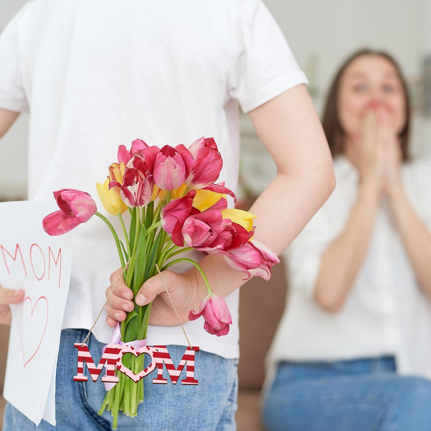 Child holding flowers with 'MOM' sign, blurred background