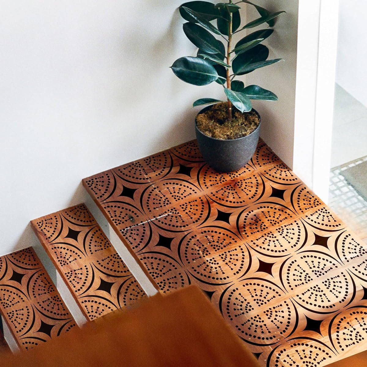 Decorative tiles with geometric patterns on a floor next to a potted plant.