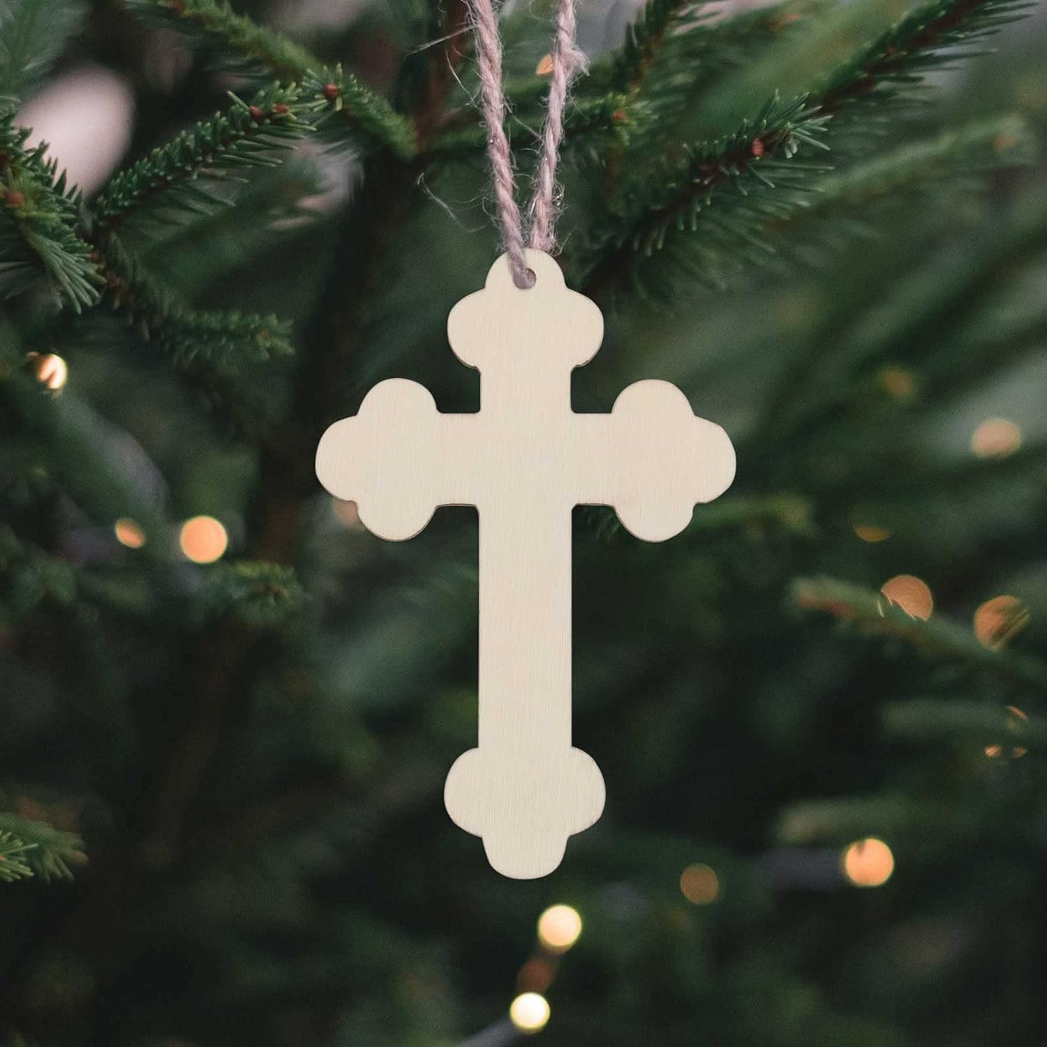 Decorative cross hanging on a Christmas tree with blurred lights in the background