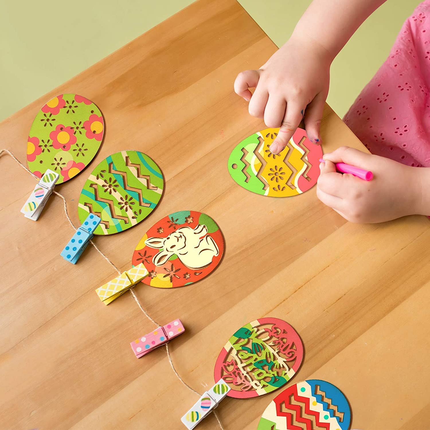 Colorful paper crafts on a wooden table with a child's hands using a pink marker.