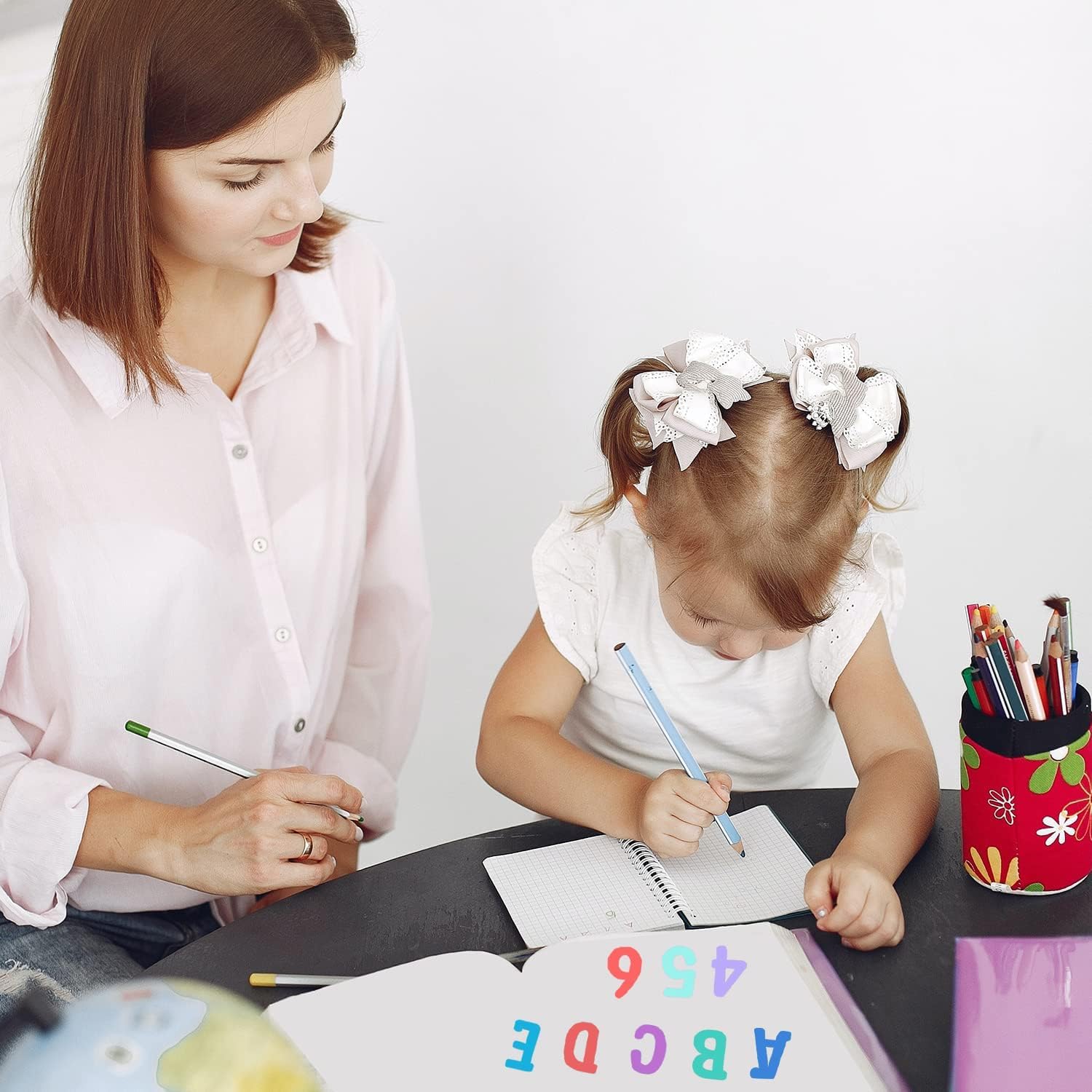 Woman and young girl sitting at a table with writing materials, focusing on education or learning.