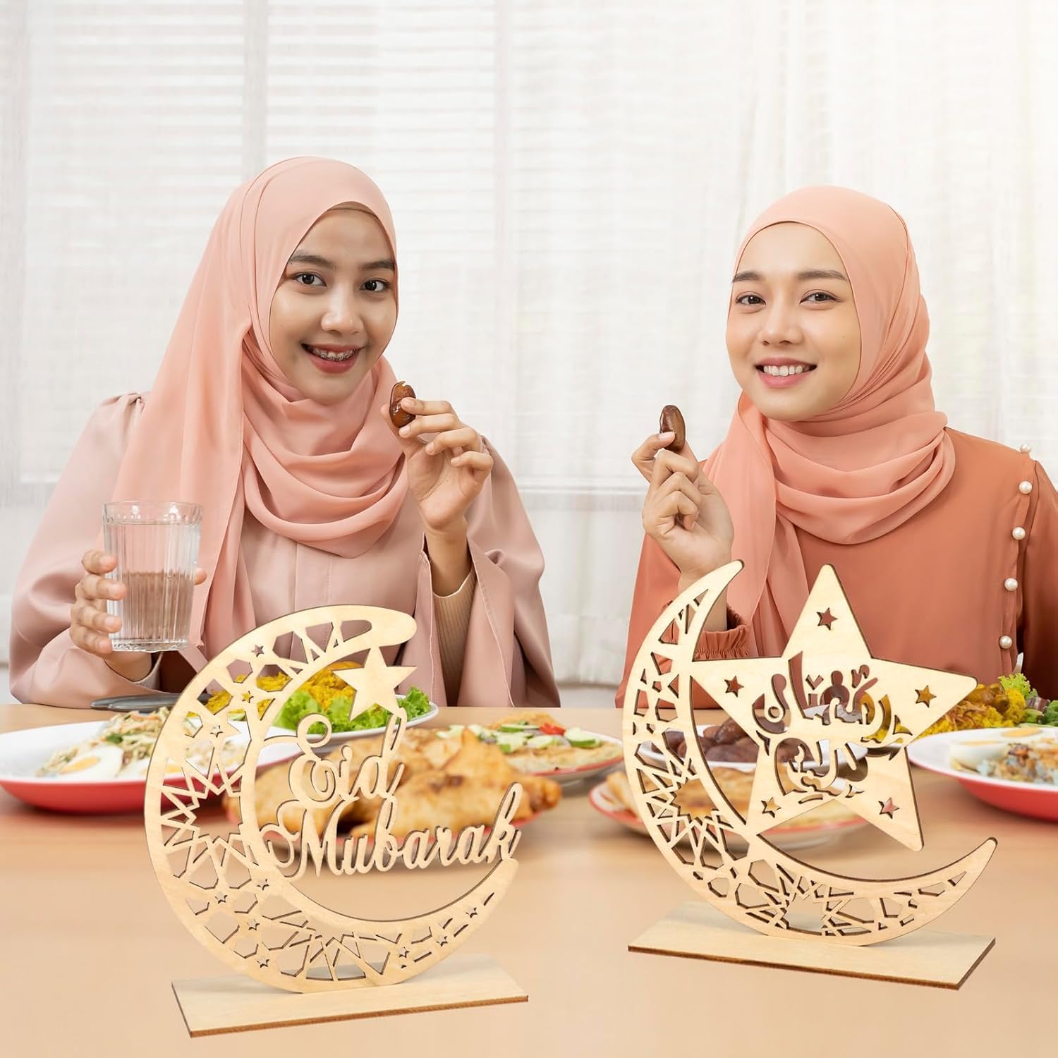 Two women sitting at a table with 'Oid Mubarak' decorations during a meal.