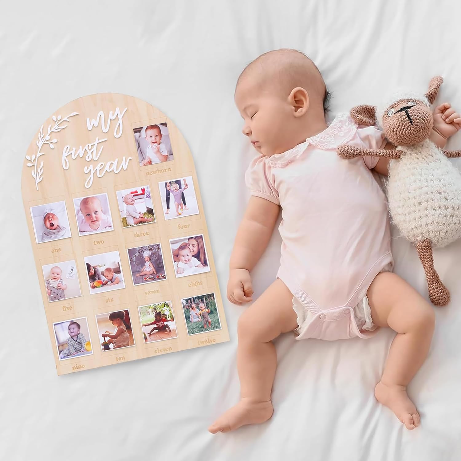 Baby lying next to a 'My First Year' photo display with stuffed animals on a white blanket.