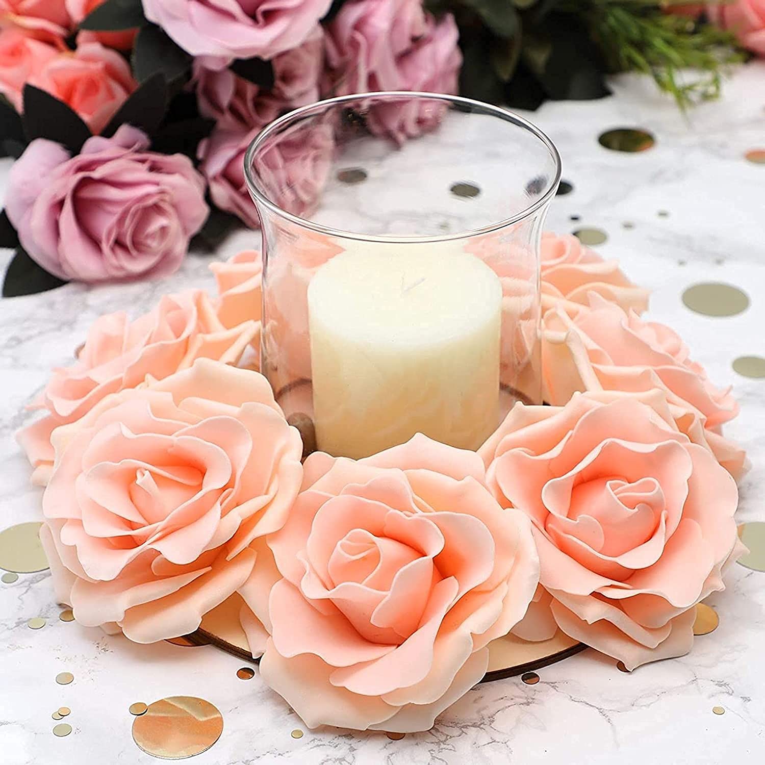 Decorative arrangement of peach roses with a candle in the center on a white surface.