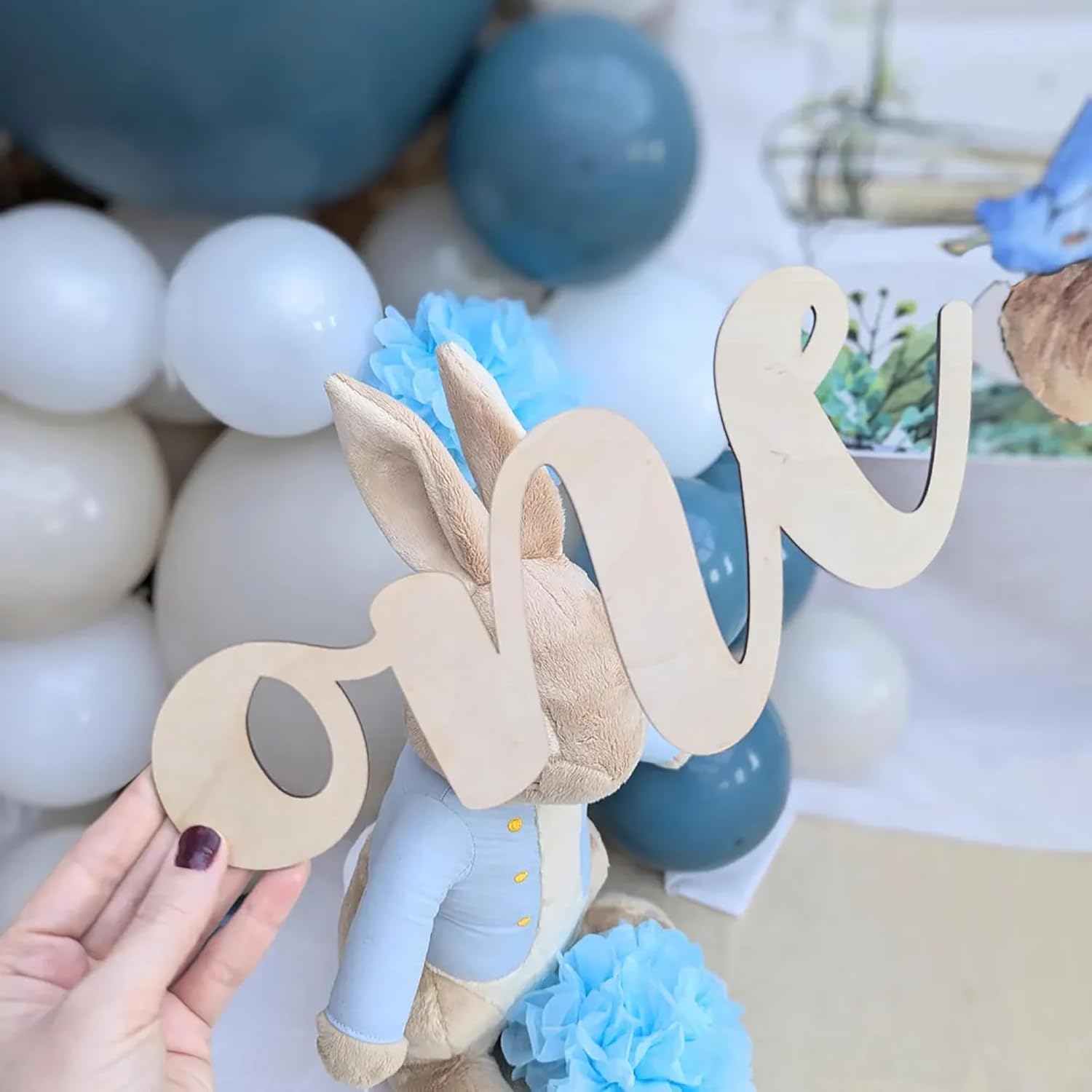 Wooden number 'one' with a plush toy elephant against a backdrop of balloons and decorations.