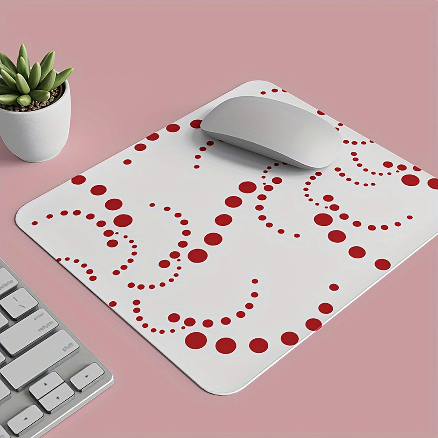 White mouse pad with red heart pattern on a pink surface, accompanied by a keyboard and a small plant.