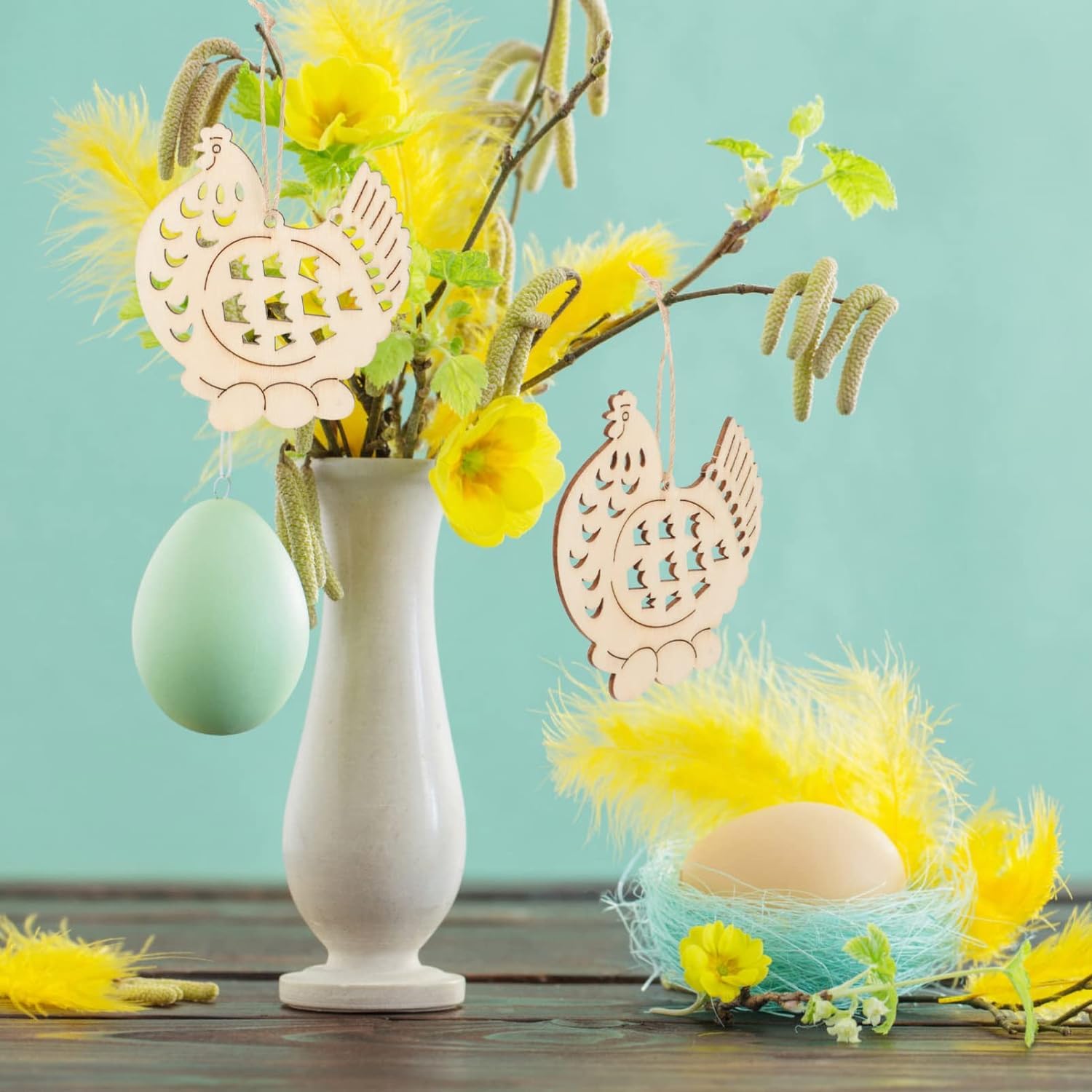 Decorative Easter setup with a vase, eggs, and wooden dove ornaments on a teal background.