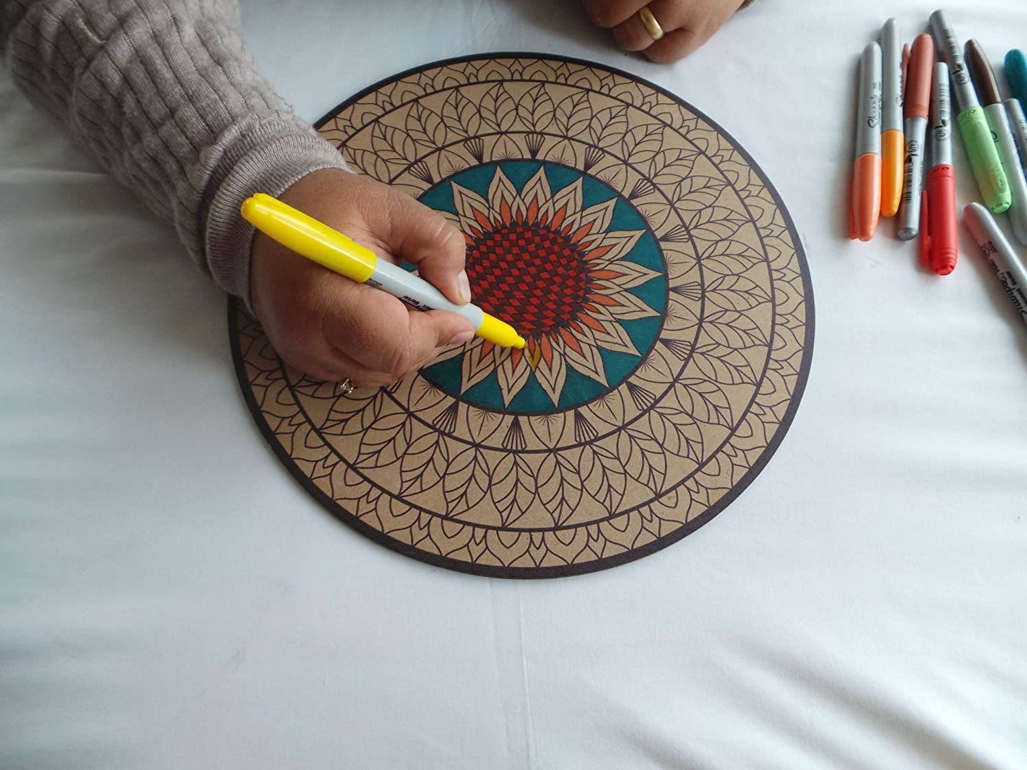 Person coloring a mandala design on a round wooden board with markers.