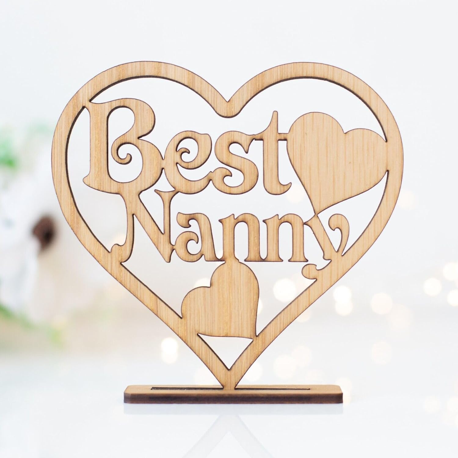 Wooden heart-shaped decoration with 'Best Nanny' text on a blurred background