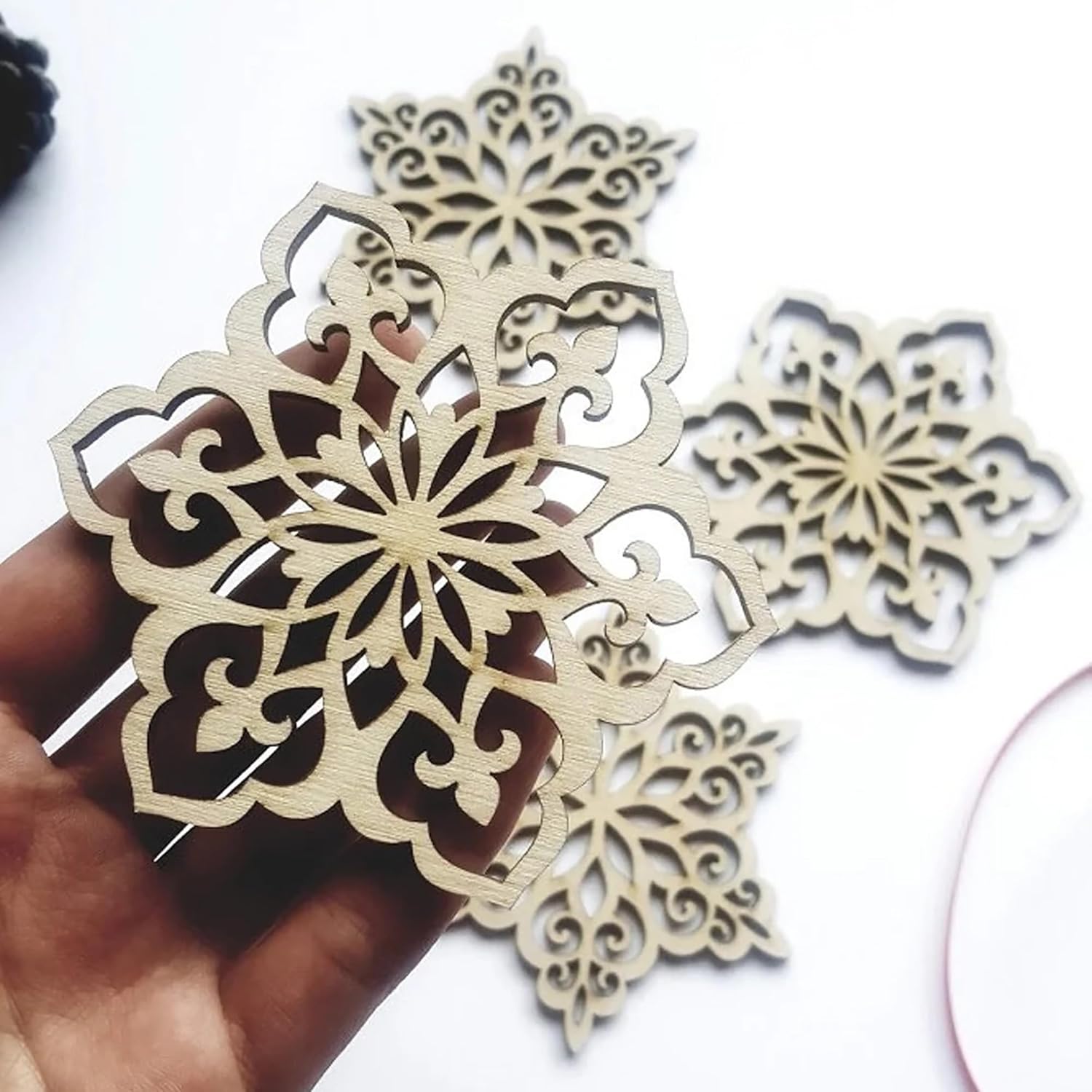 Decorative wooden snowflake cutouts held by a hand on a white background