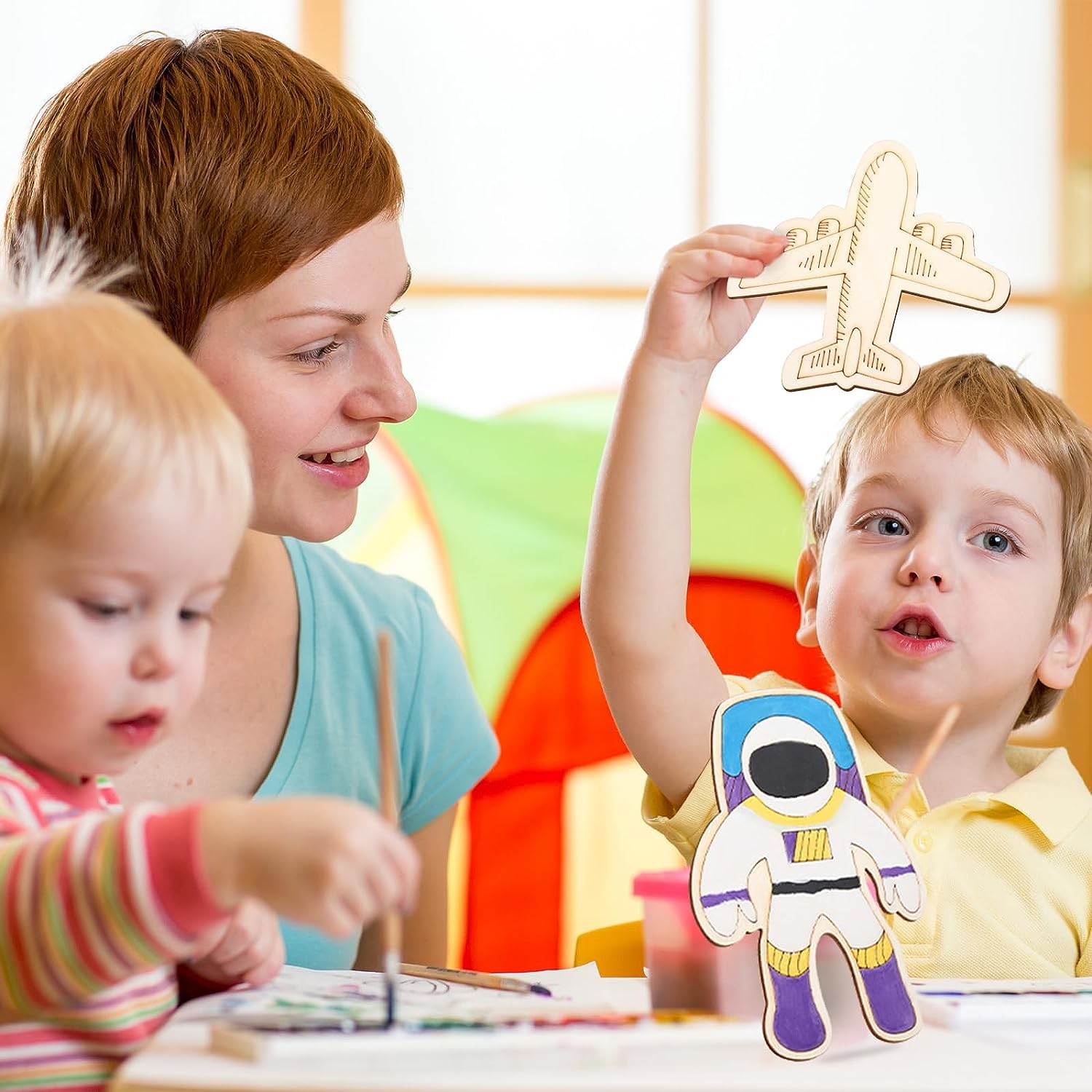 Woman and two children in a colorful room with craft materials and toys.