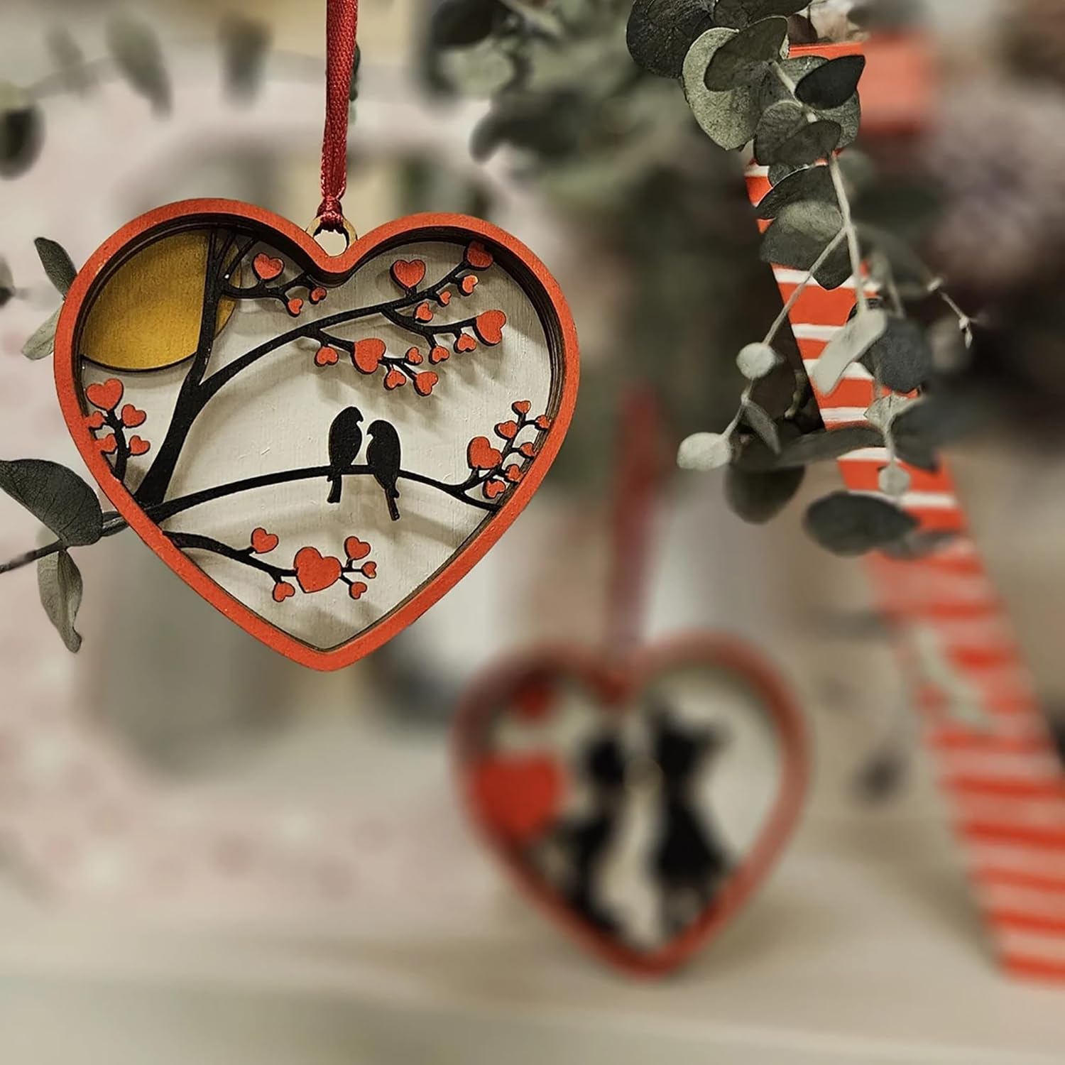 Heart-shaped ornament with tree and birds design, hanging against a blurred natural background.