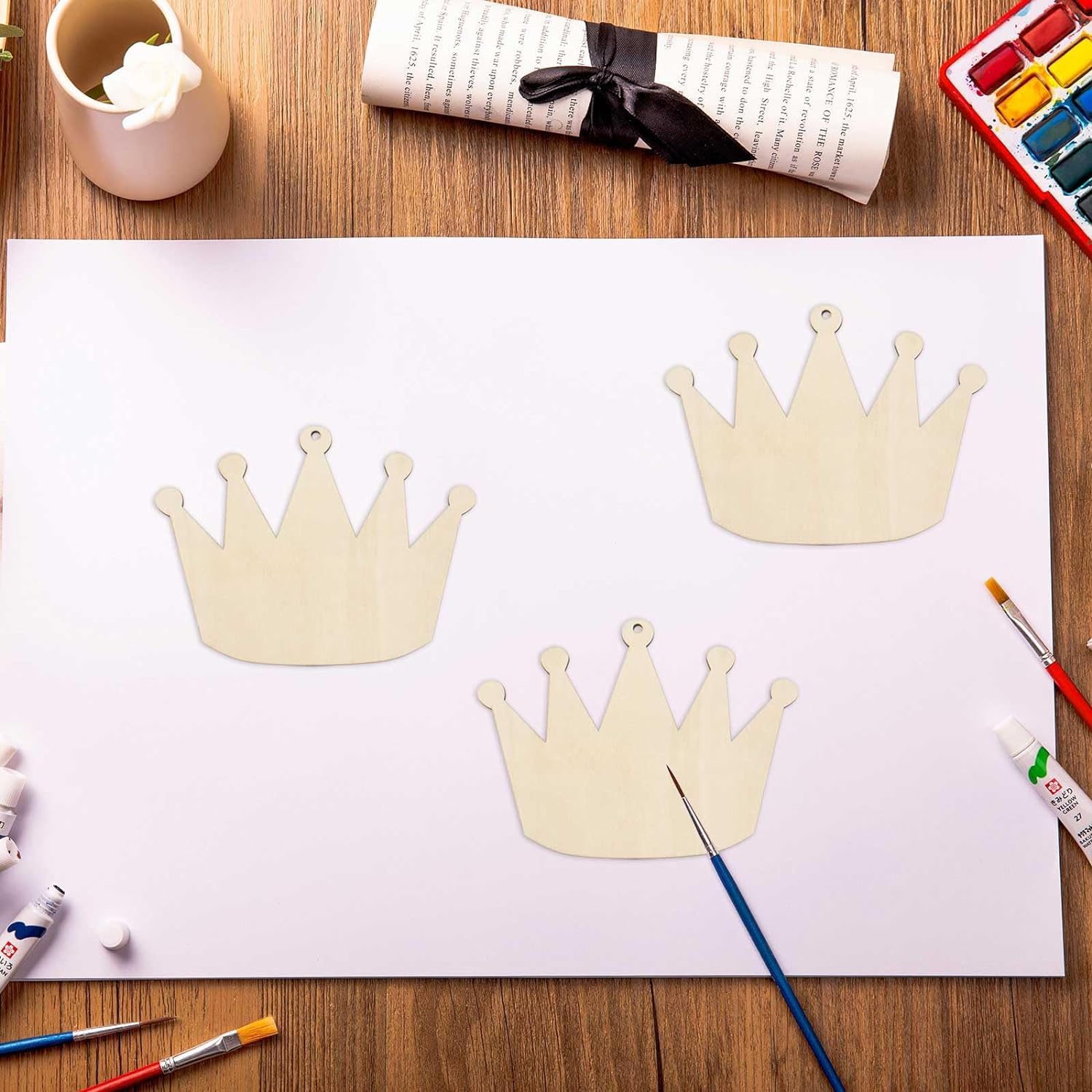 Three cardboard crowns on a piece of paper with art supplies on a wooden table.