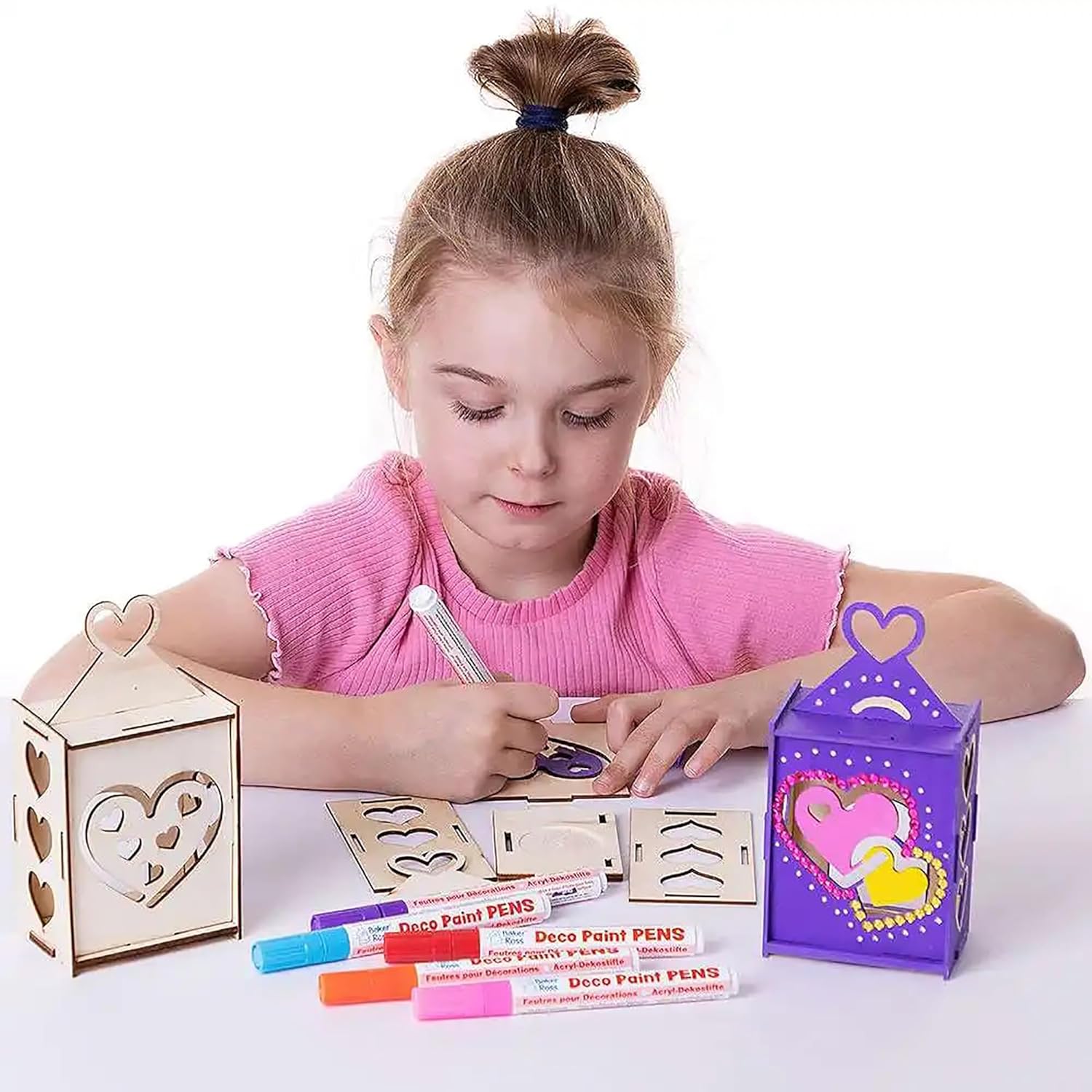 Young girl crafting with wooden heart-shaped lantern and markers on a white background