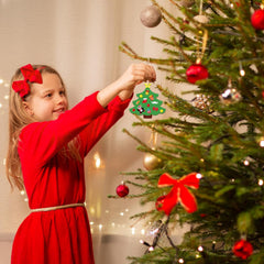 Child in a red dress decorating a Christmas tree with ornaments.