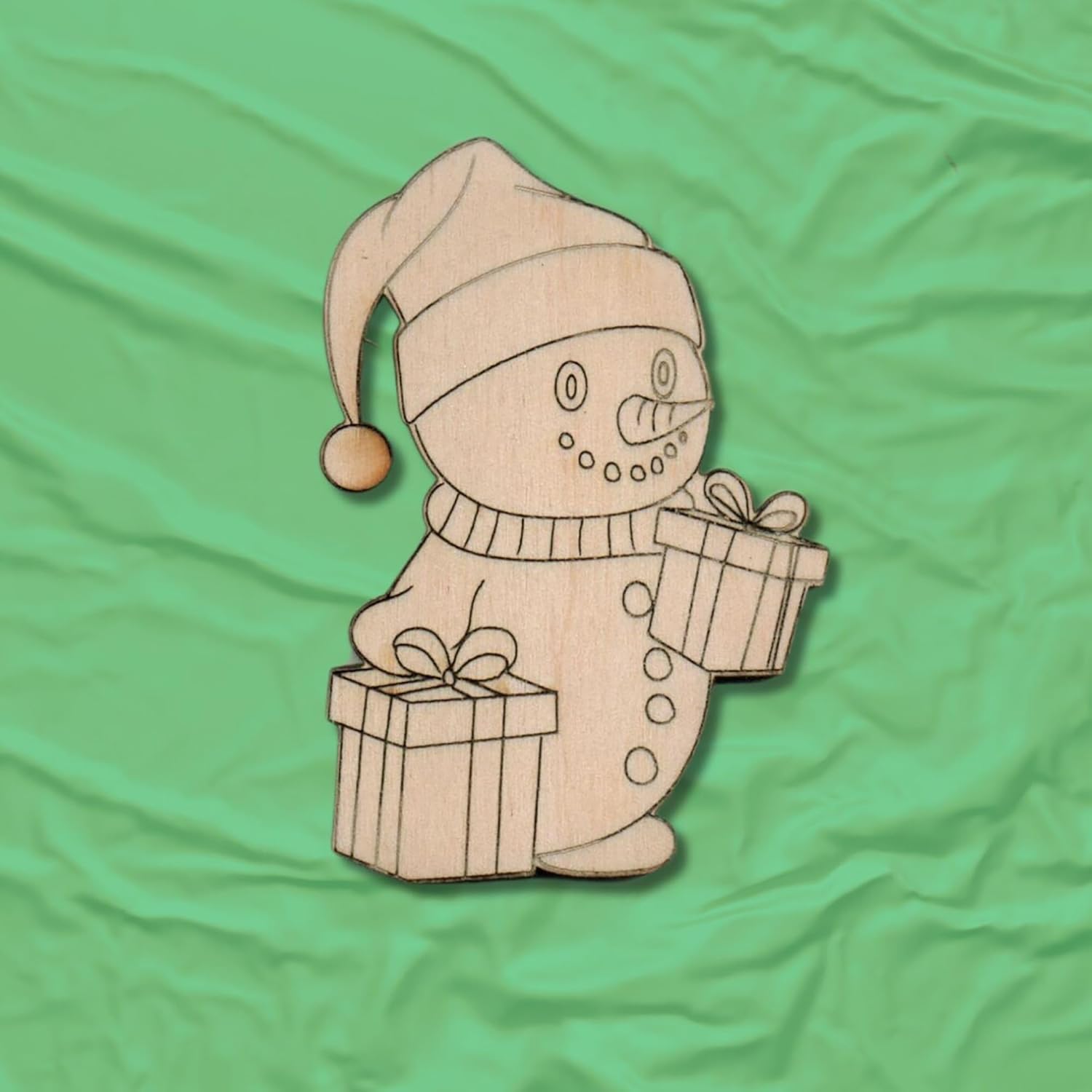 Wooden snowman figurine with a gift on a green fabric background