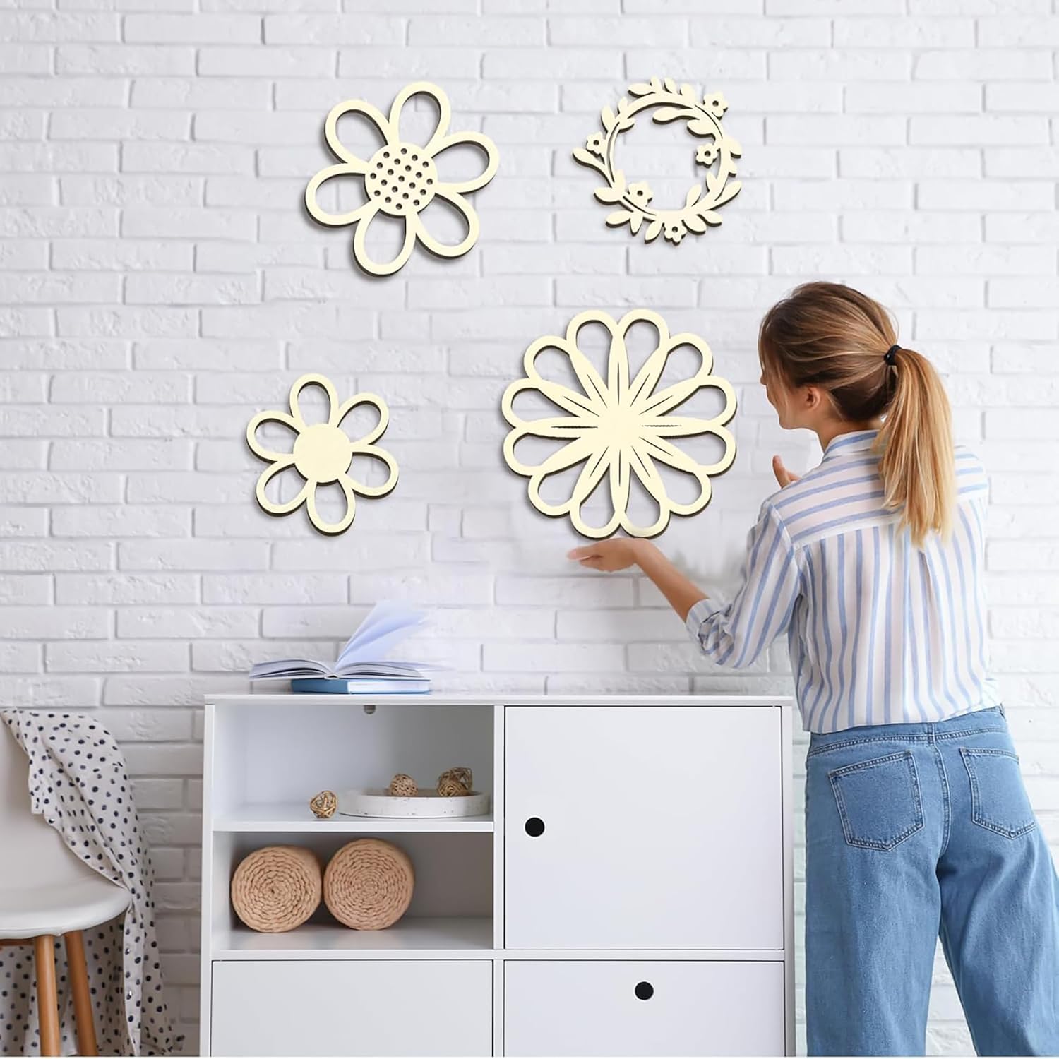 Woman arranging decorative wall art on a white brick wall
