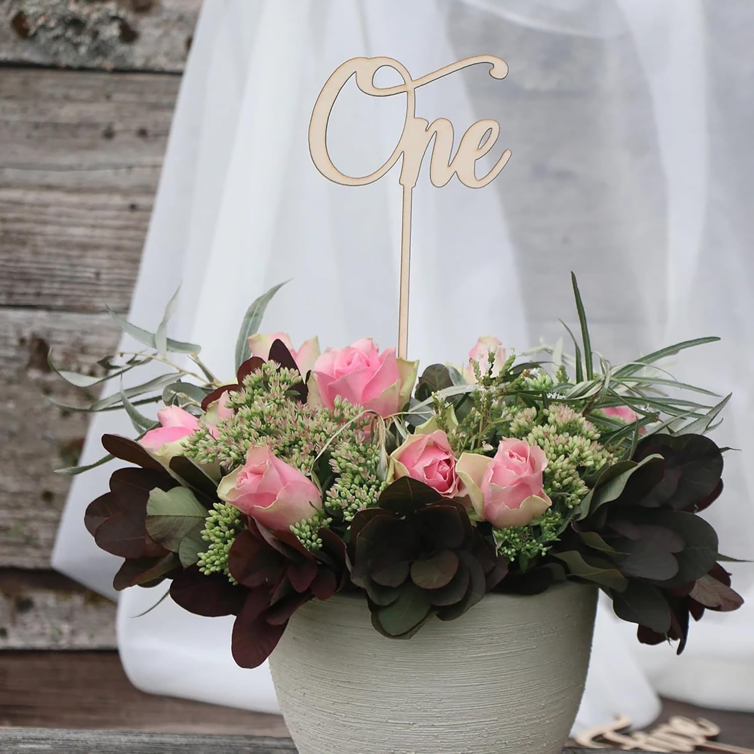 Floral arrangement with a 'One' cake topper on a wooden surface.