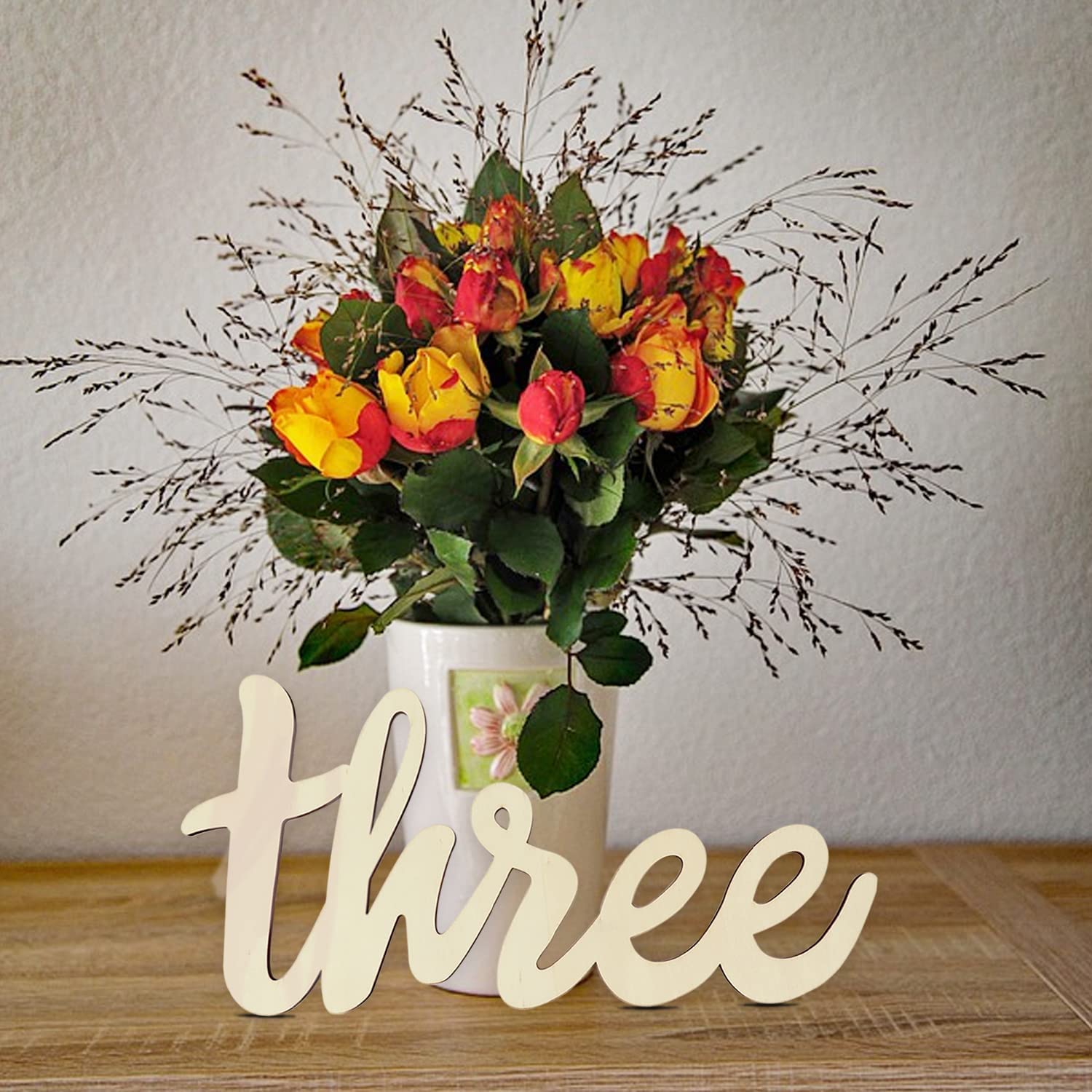 Bouquet of red and yellow flowers in a vase with a wooden number 'three' on a wooden surface.