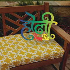 Colorful decorative item with 'Happy Holi' text on a yellow cushioned chair outdoors.