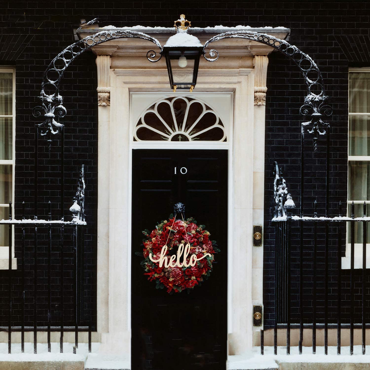 Black door with a wreath and 'hello' sign, flanked by black brick buildings.