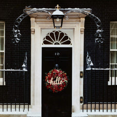 Black door with a wreath and 'hello' sign, flanked by black brick buildings.