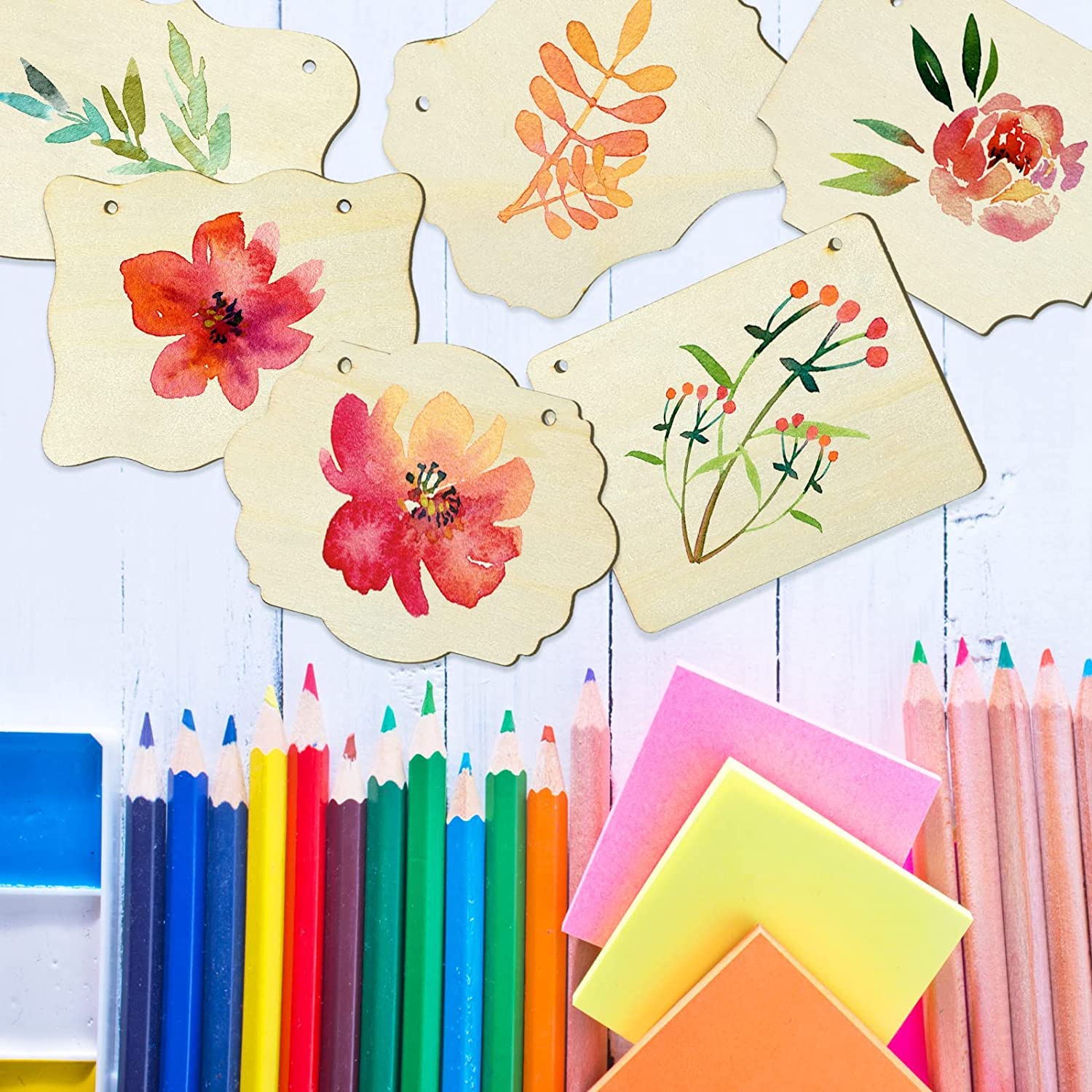 Decorative wooden tags with floral designs and colorful stationery items on a white surface.