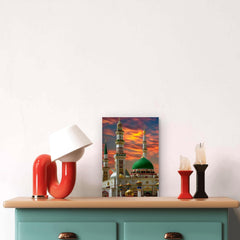 Decorative setup with a painting of a mosque, red and black lamps, and candles on a light-colored surface.